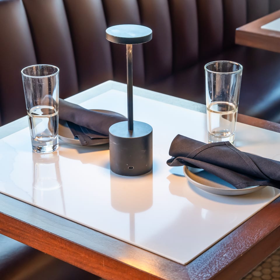 Elegant restaurant table set with two water glasses, folded black napkins, and a central candleholder in a booth.