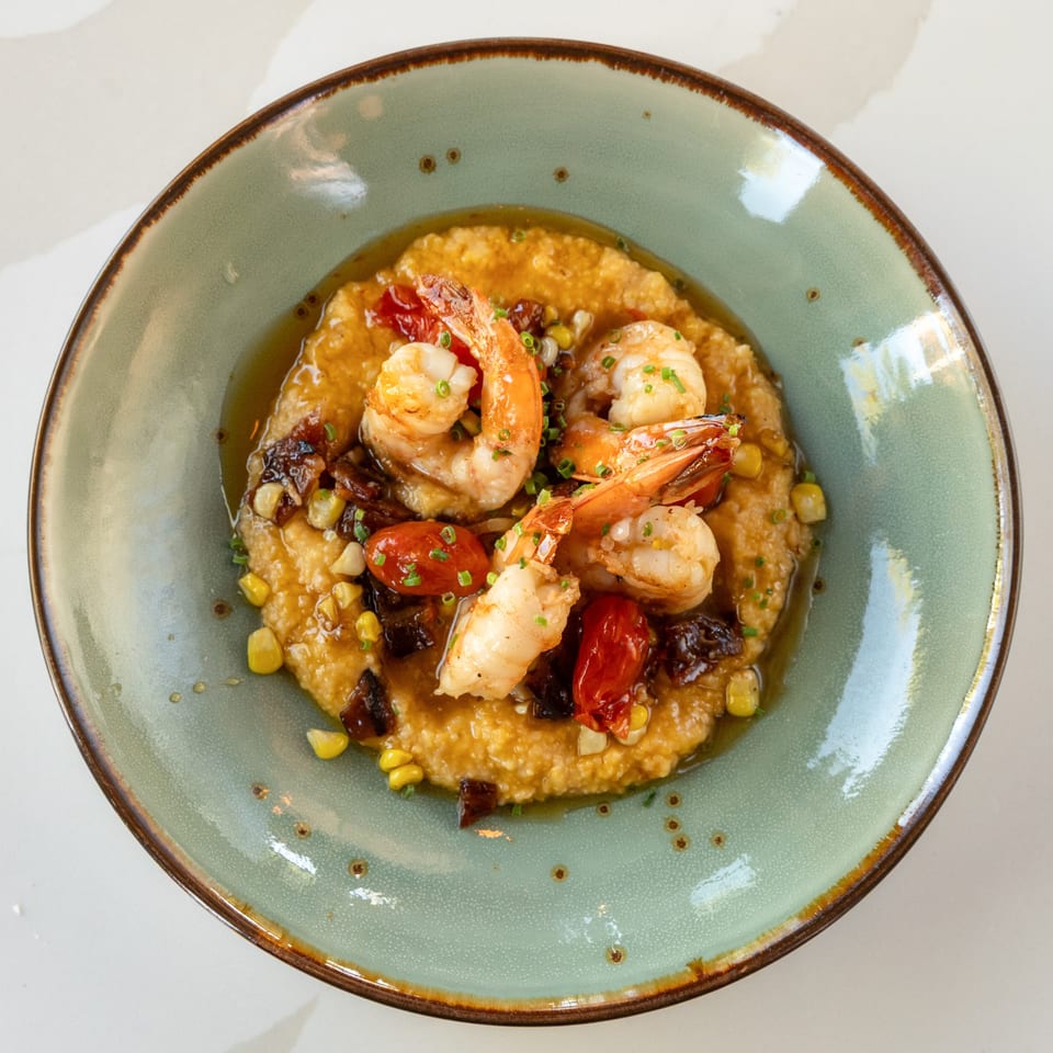 Overhead view of shrimp served over creamy grits with roasted tomatoes, corn, mushrooms, and chives on a green ceramic plate.
