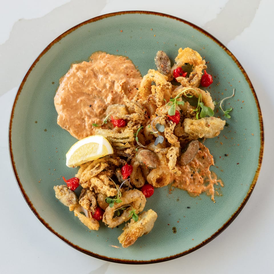 Crispy fried seafood with lemon, red peppers, microgreens, and creamy sauce on a green ceramic plate.