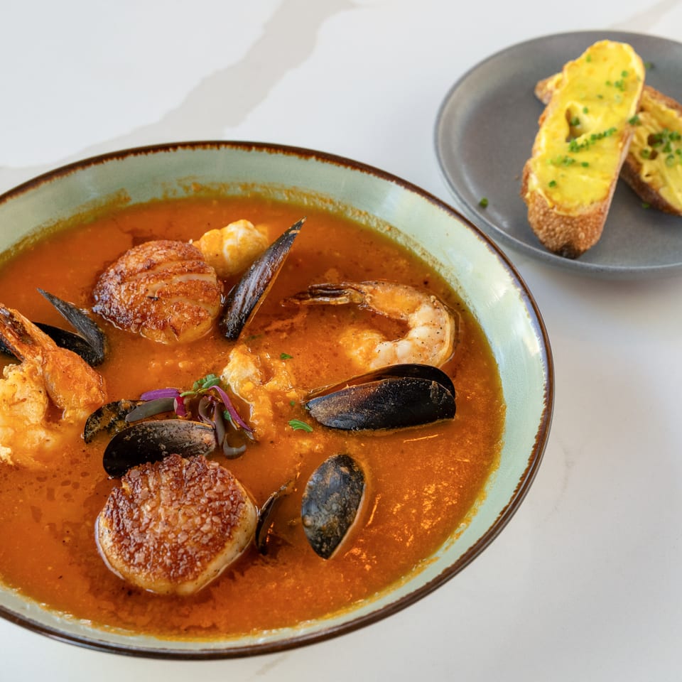 Seafood stew with shrimp, mussels, scallops, and fish in tomato broth, served with cheesy toasted bread.