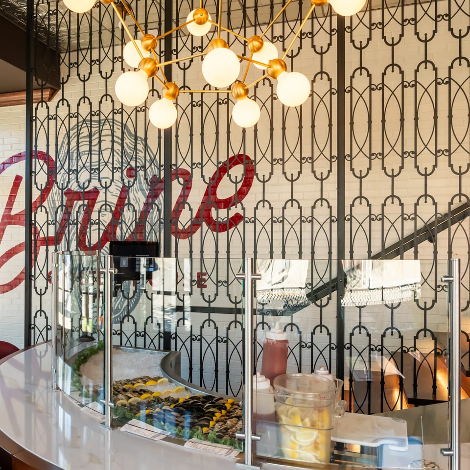 Elegant restaurant interior with oyster display, geometric metal partition, globe chandelier, and colorful wall mural.