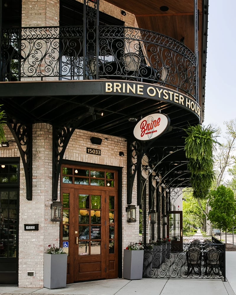 Exterior brick facade with decorative wrought iron balcony and signage featured on the about Brine Oyster House page