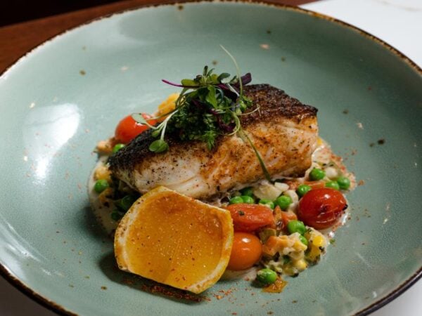 Pan-seared Alaskan Halibut served over summer succotash with confit heirloom cherry tomatoes, microgreens, and a charred lemon slice at Brine Oyster House.